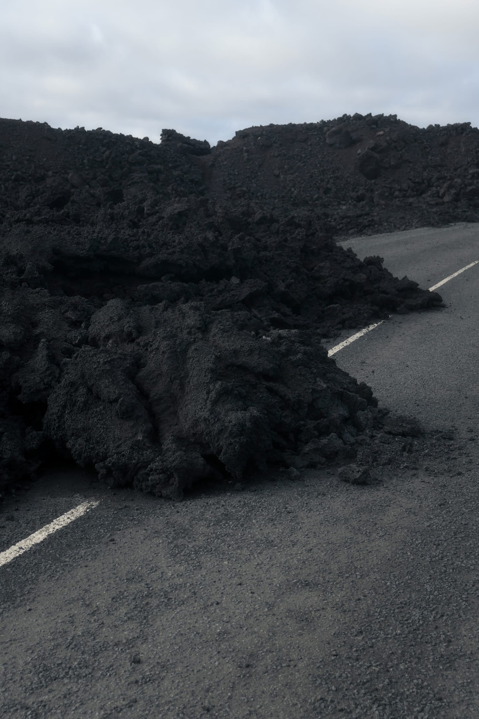 a field of black lava rock beside an empty road under a pale sky