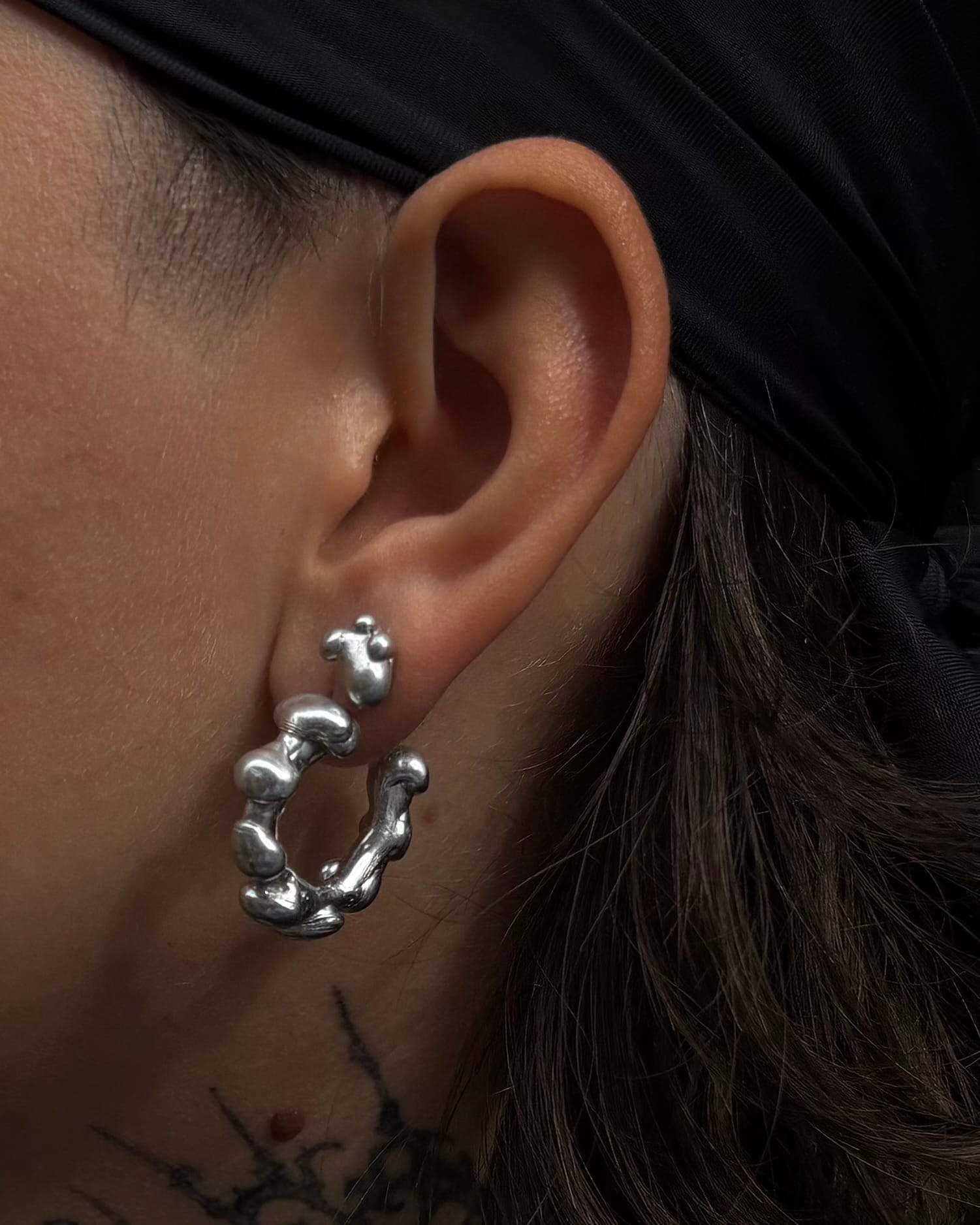 close-up of an ear wearing a molten, beaded silver hoop