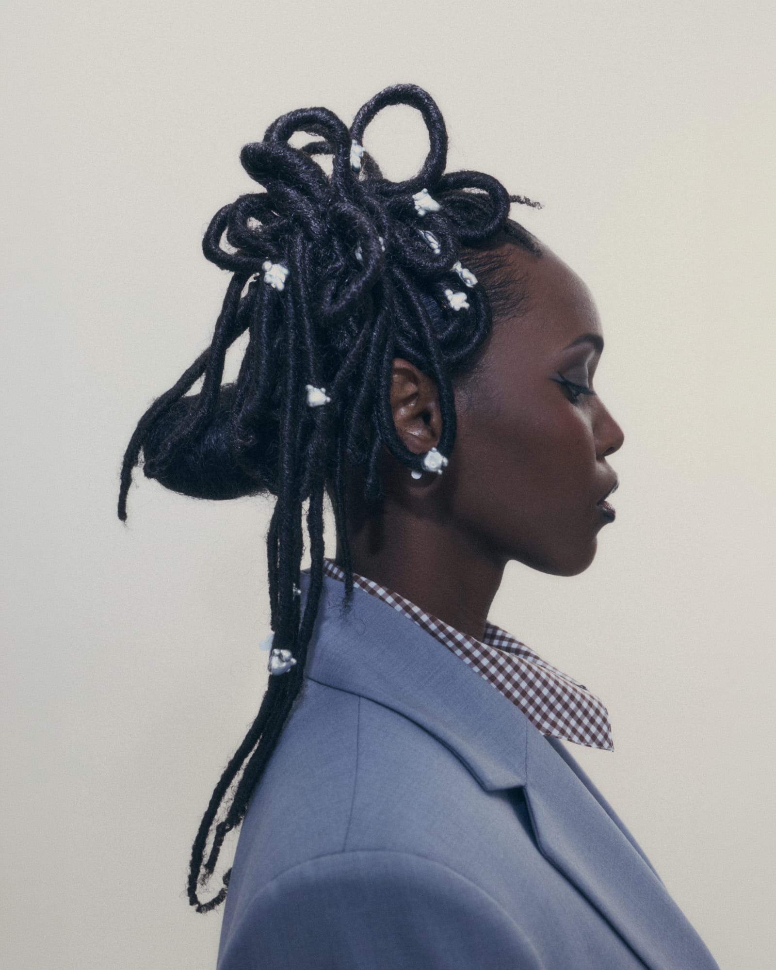 profile of a person in a pale blue blazer, small silver pieces threaded through their locs