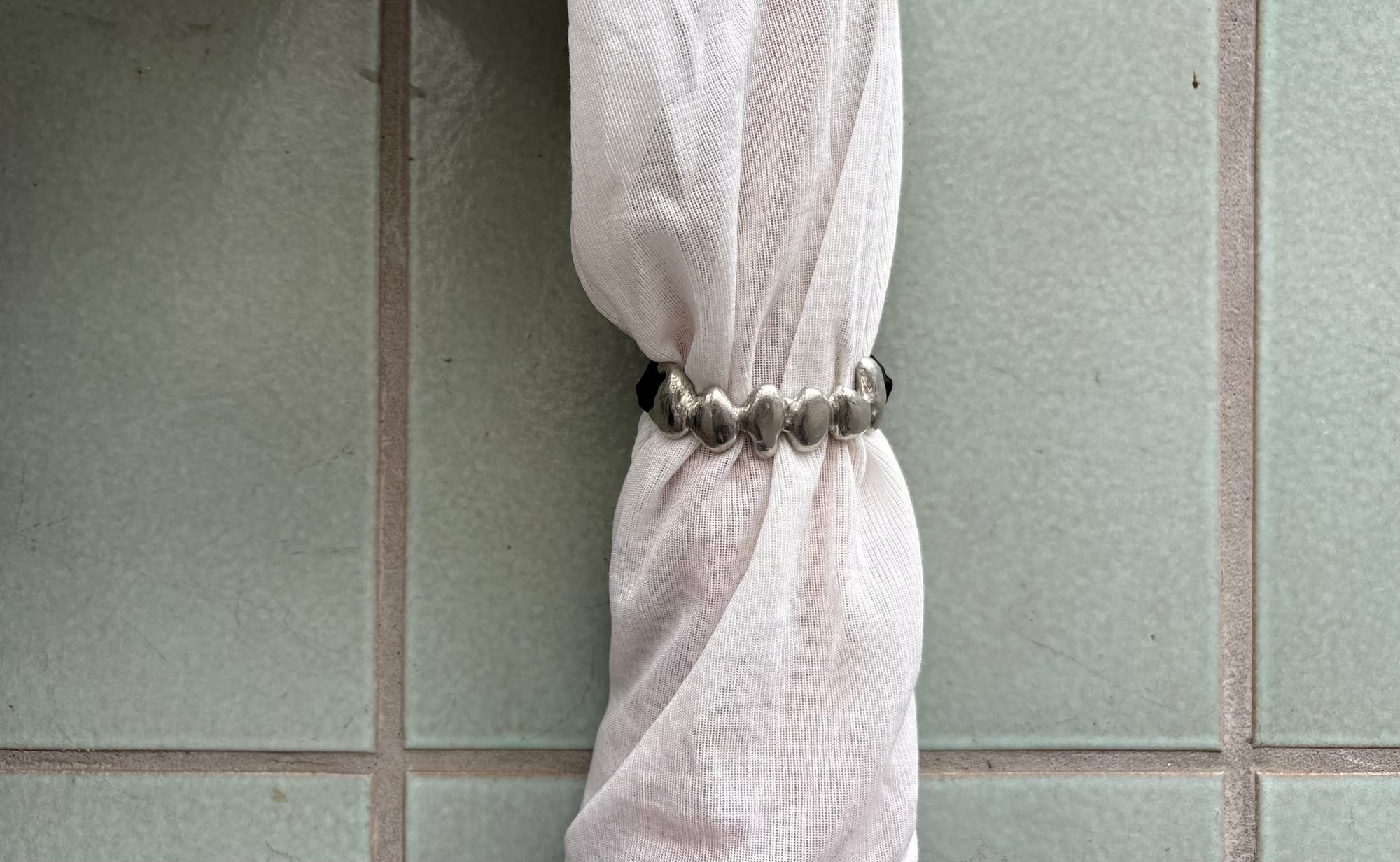 a beaded silver bracelet gathering a white sleeve against green tiles